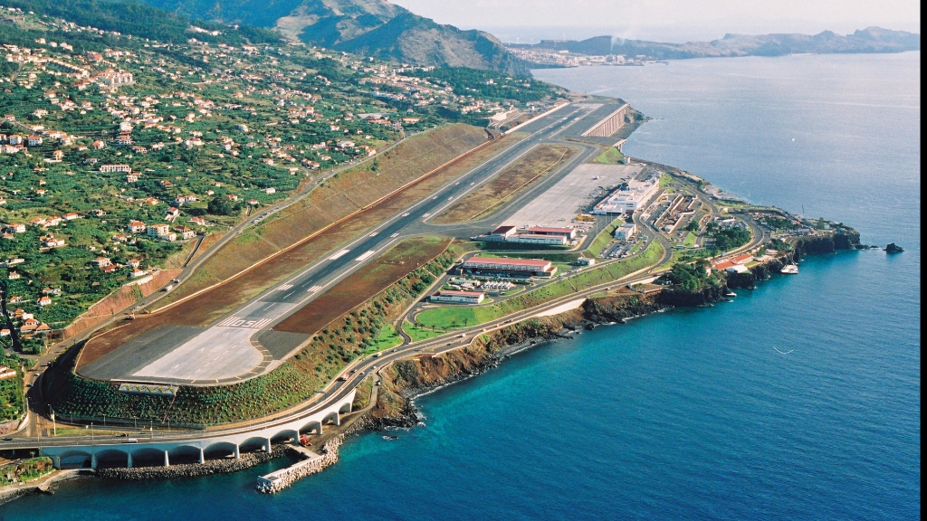 Commercial airplane preparing to land at a challenging coastal airport surrounded by hills and water